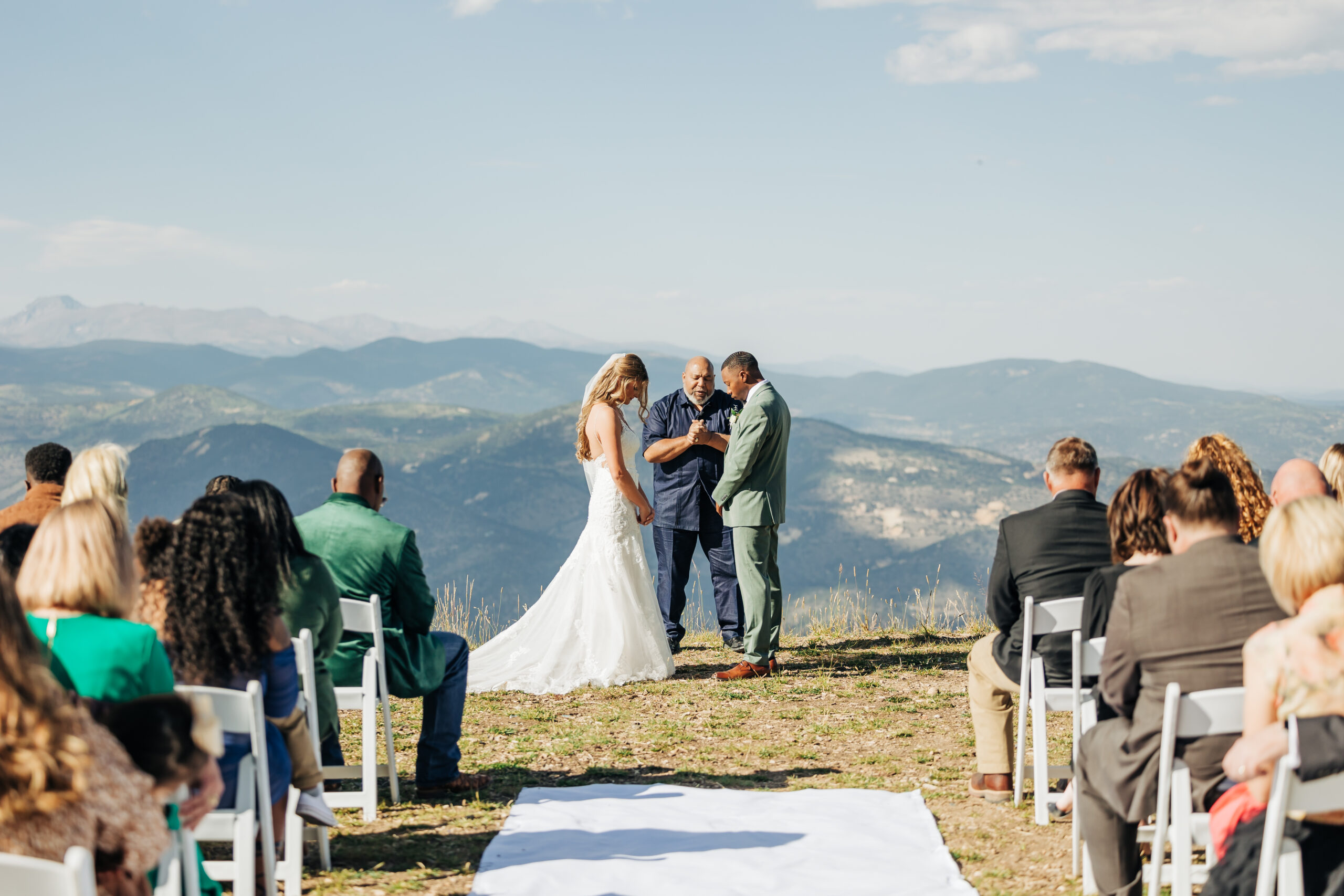 A couple stands hand in hand at their Colorado mountain wedding ceremony, surrounded by loved ones and framed by sweeping alpine views under a clear blue sky.