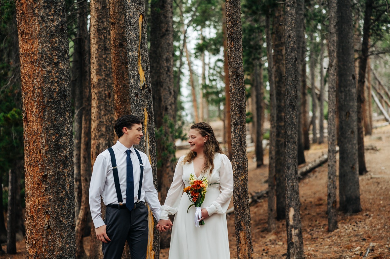 Newly married couple smiles at each other while holding hands in a peaceful Colorado forest.