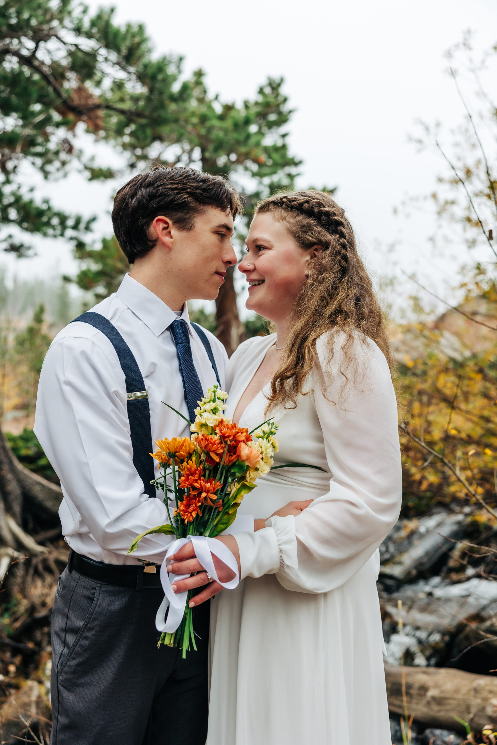 Bride and groom share a quiet moment, holding a rustic bouquet with orange and yellow blooms.