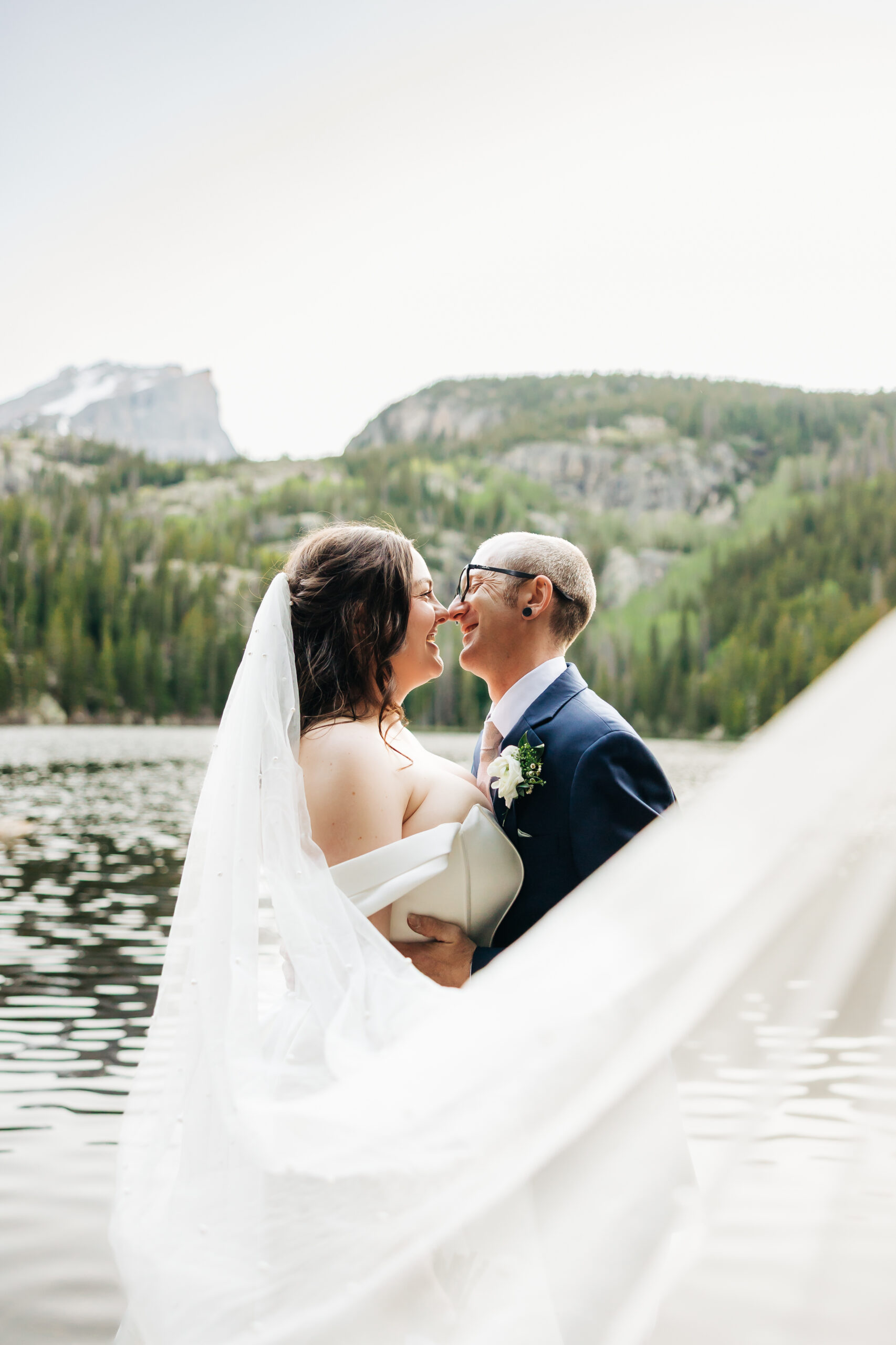 Bride looks over her shoulder while embracing her partner during a quiet moment surrounded by tall forest trees