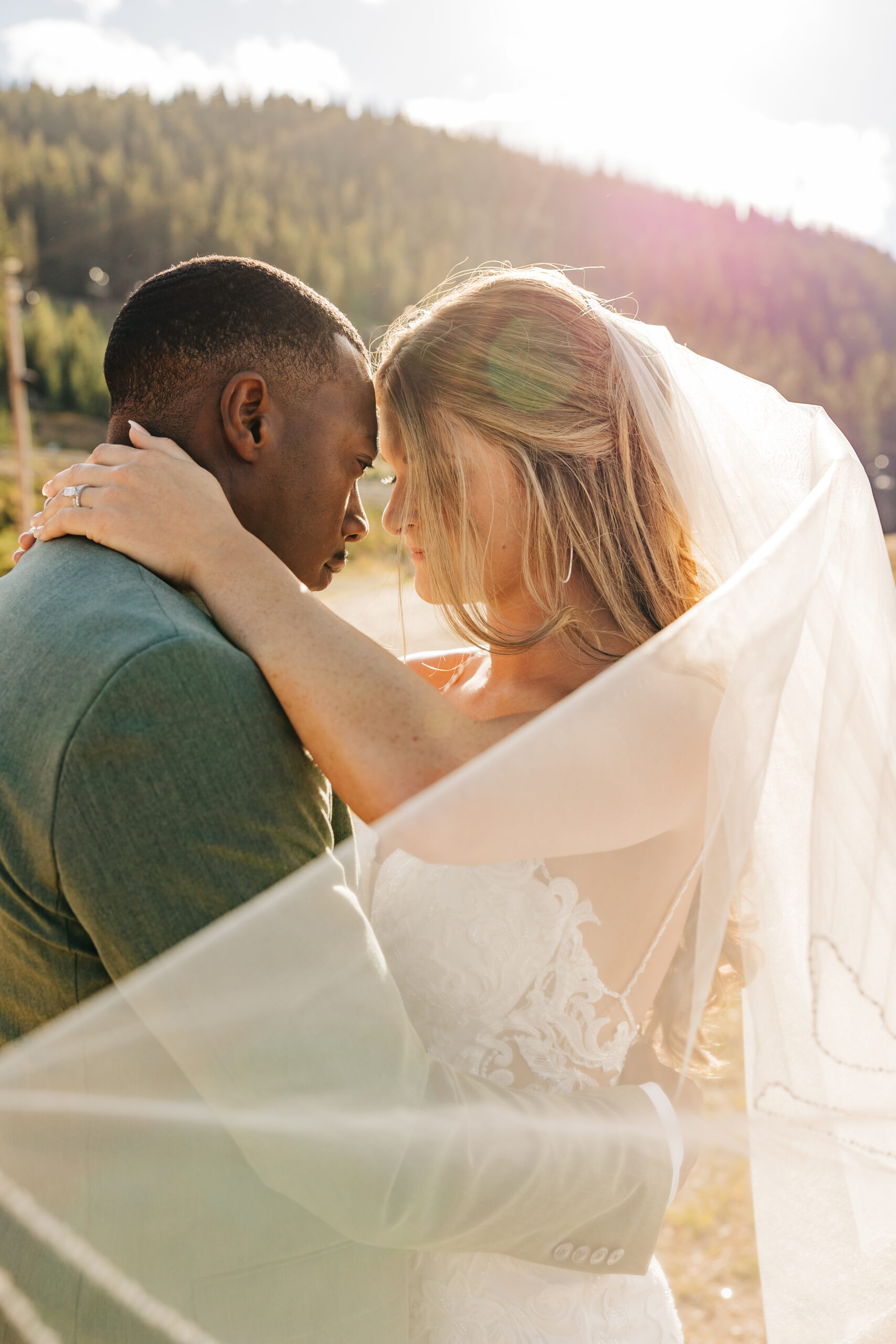 Bride and groom share a quiet, emotional moment wrapped in her veil after their heartfelt Colorado mountain wedding.