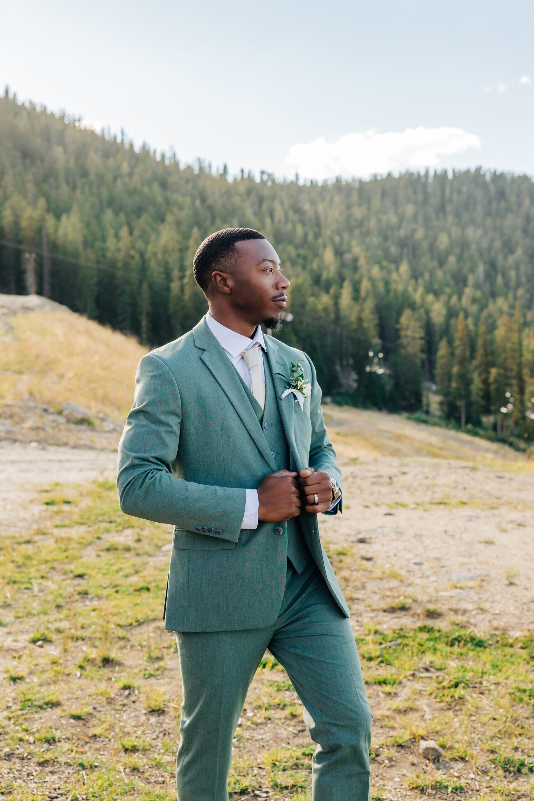 Groom stands alone adjusting his jacket, captured in the warm light of day during Colorado wedding photos.