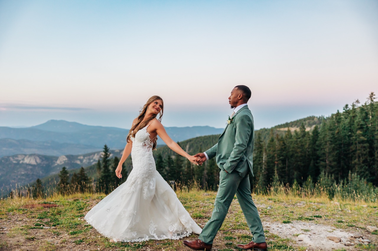 Playful moment between bride and groom as they walk through wildflower-covered terrain after their Colorado mountain wedding.
