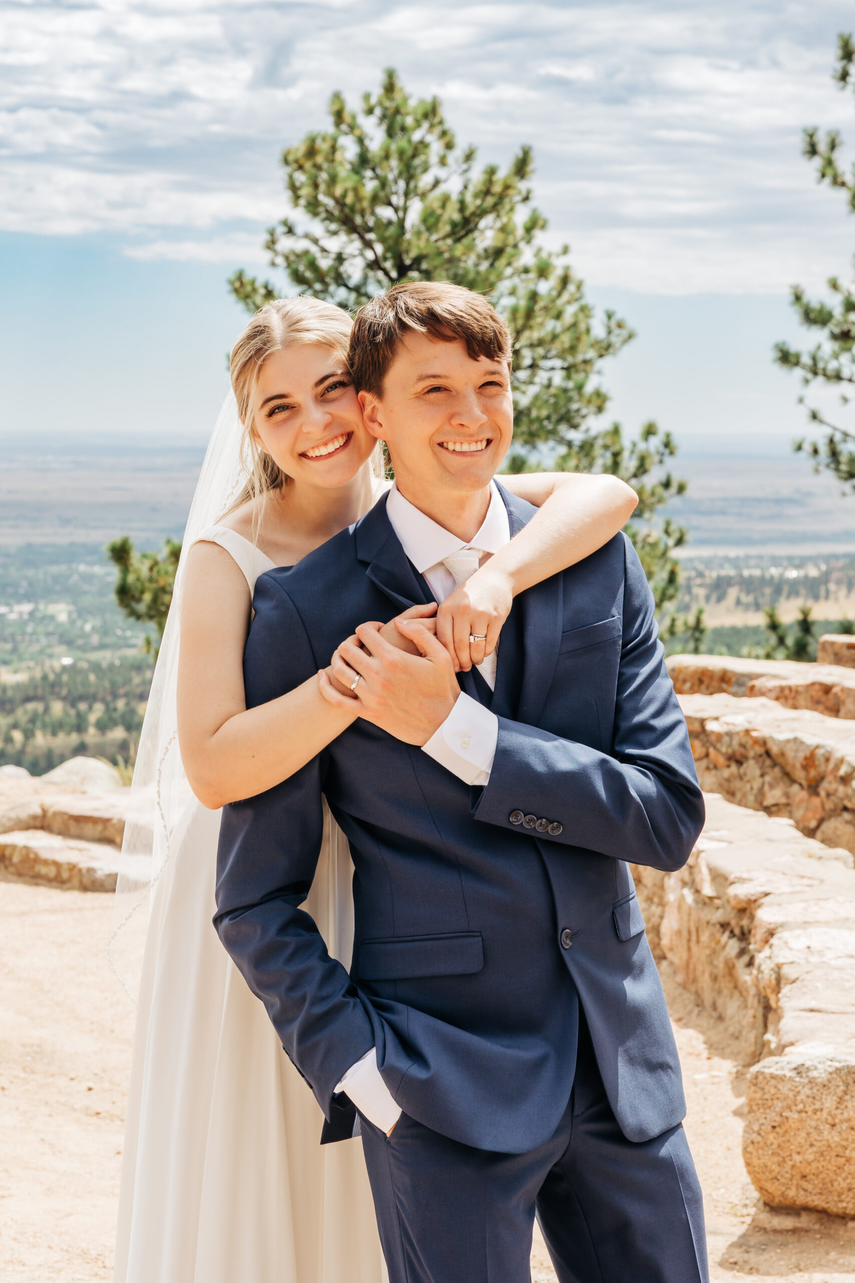 Bride wraps her arms around the groom in a sweet embrace with pine trees and valley views behind them—an intimate portrait from their wedding day hike.