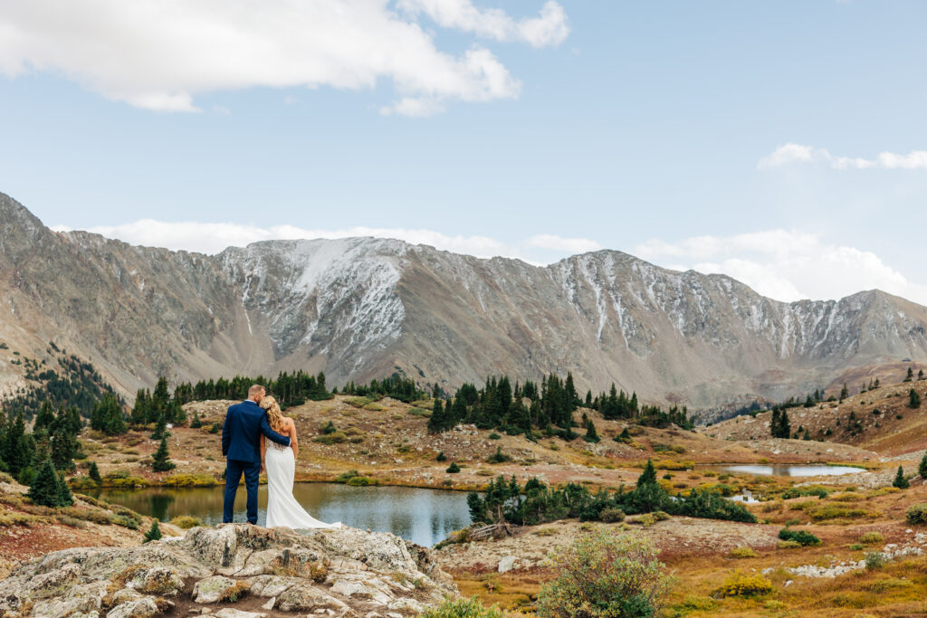 couple standing together holding each other surrounded by mountains with a lake