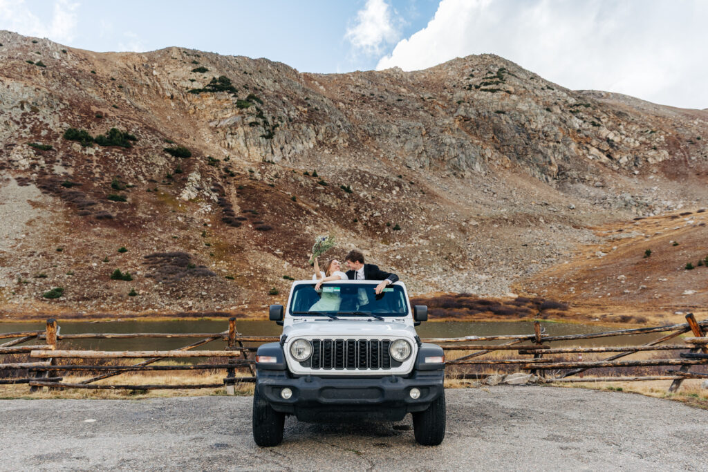 couple standing inside a jeep with mountains behind them for their off-roading elopement