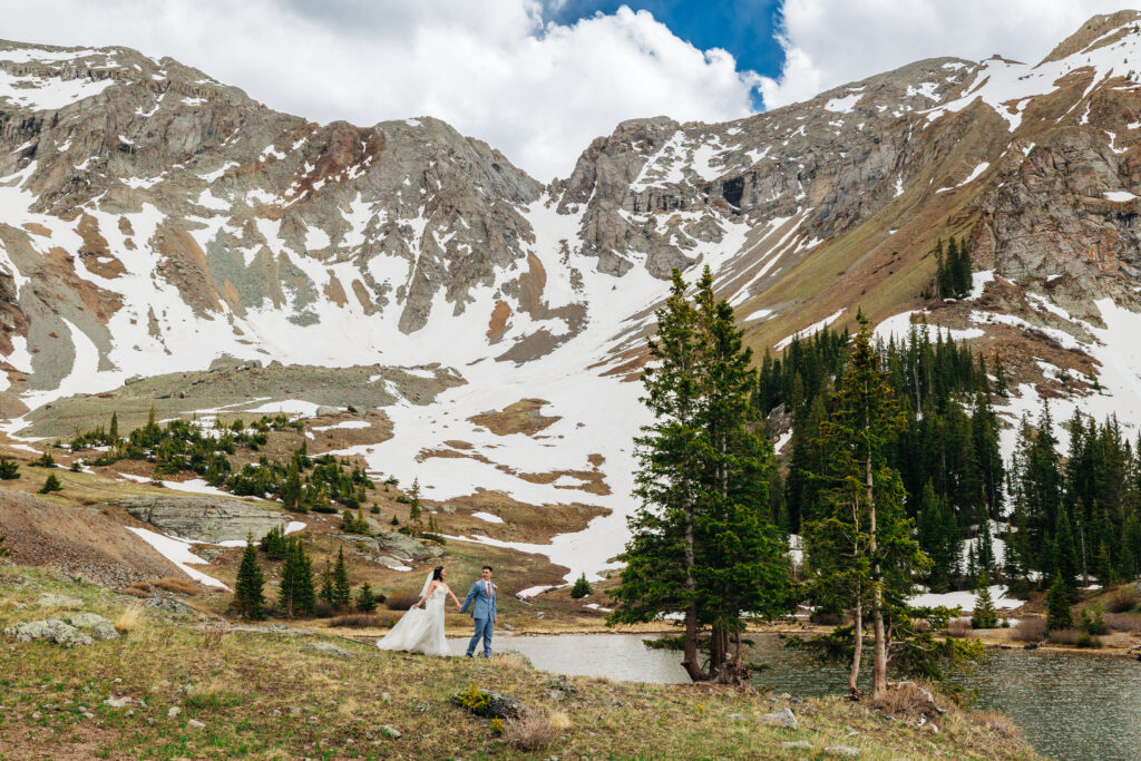 A bride and groom walking together in front of a water basin with snowy mountains behind them for their off-roading elopement
