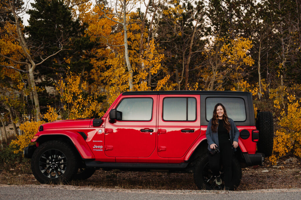 woman standing in front of a red jeep with aspen trees behind her. she is an off-roading elopement photographer