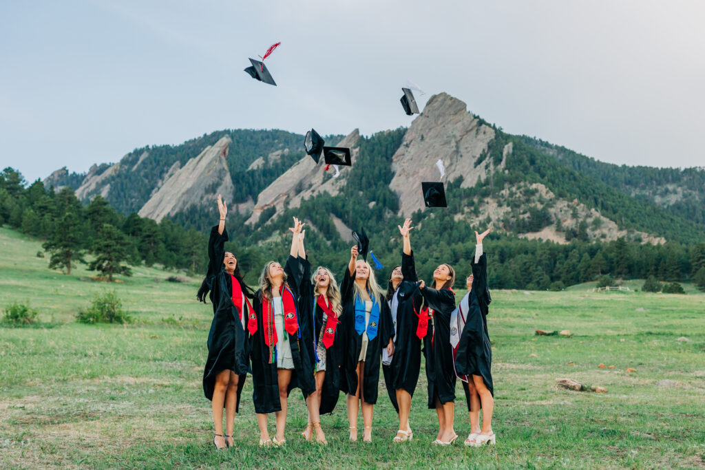 Colorado Senior Photographer captures woman with friends in field throwing caps in the air