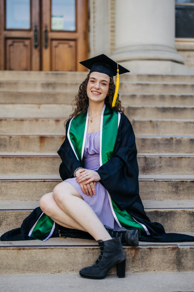 Colorado senior photographers capture woman sitting on stairs wearing graduation robes