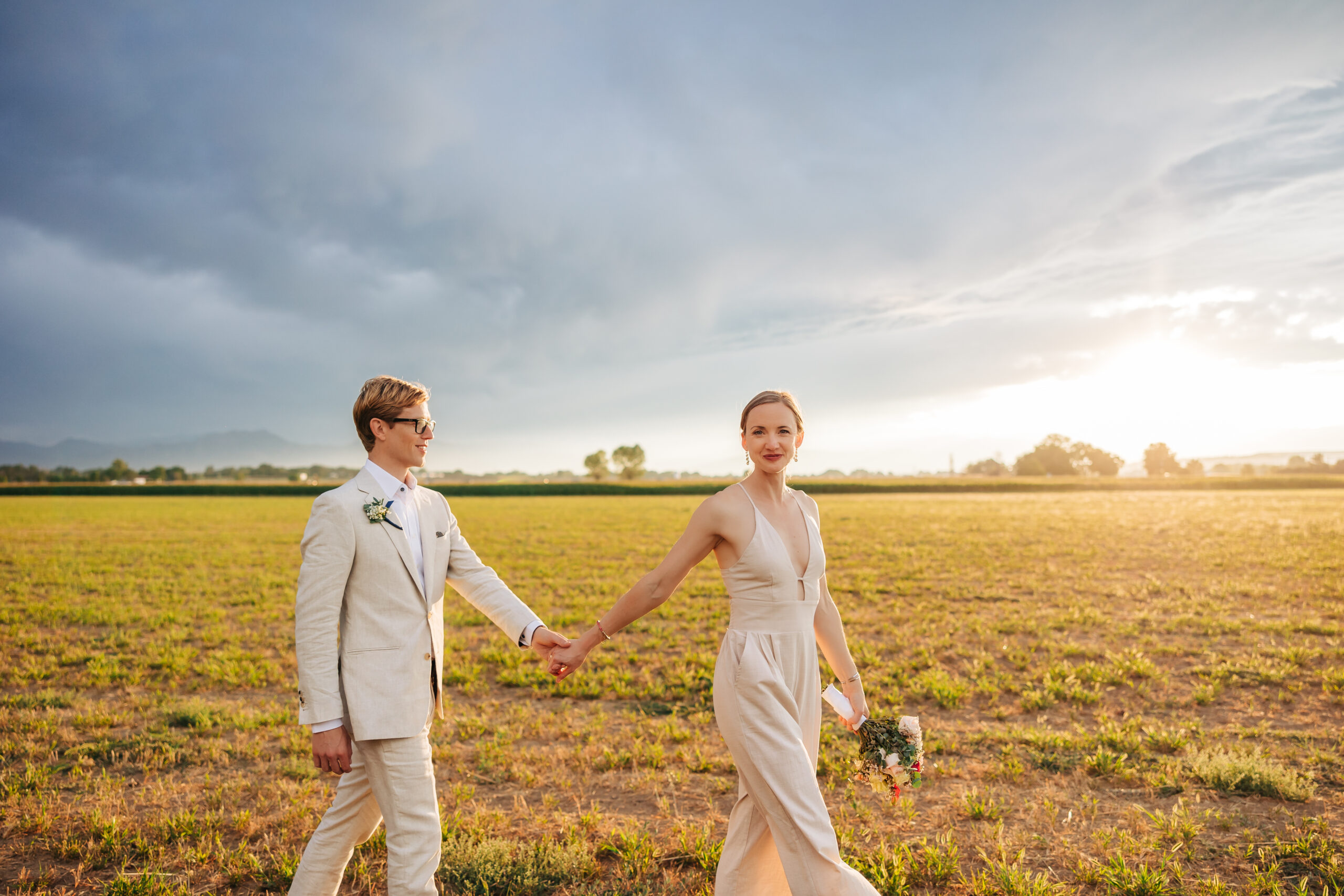 Denver Elopement Photographer captures bride and groom holding hands and walking through field