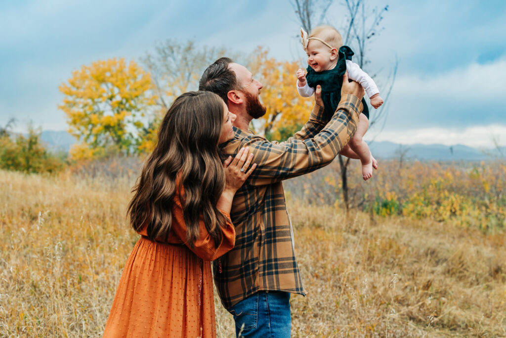 Denver Family Photographers capture father lifting baby in air while mother looks 