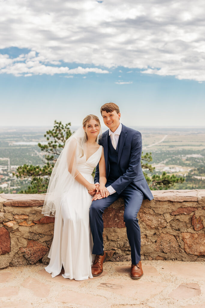 Boulder Wedding Photographer captures couple sitting on wall together as newly married couple