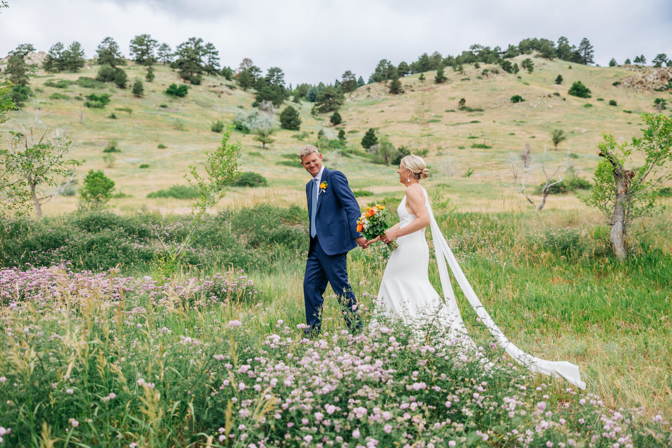 Boulder Wedding Photographer captures groom leading bride through grass after weekday wedding