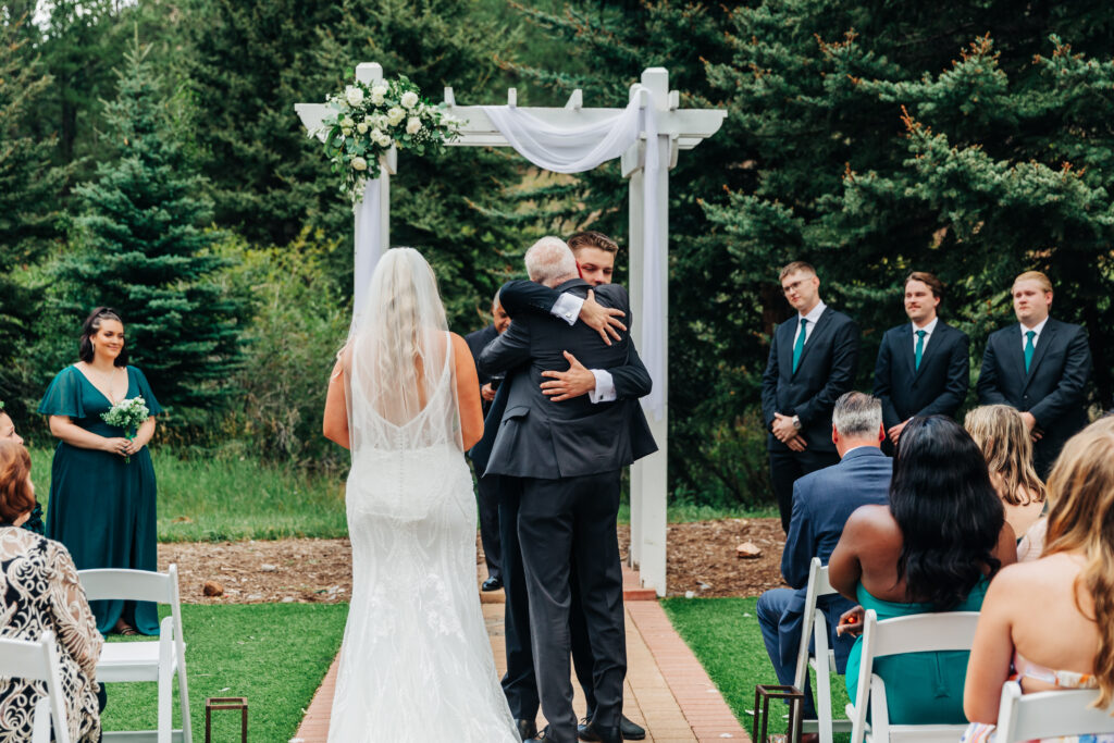 Colorado Elopement Photographer captures bride walking down aisle with father while father hugs groom