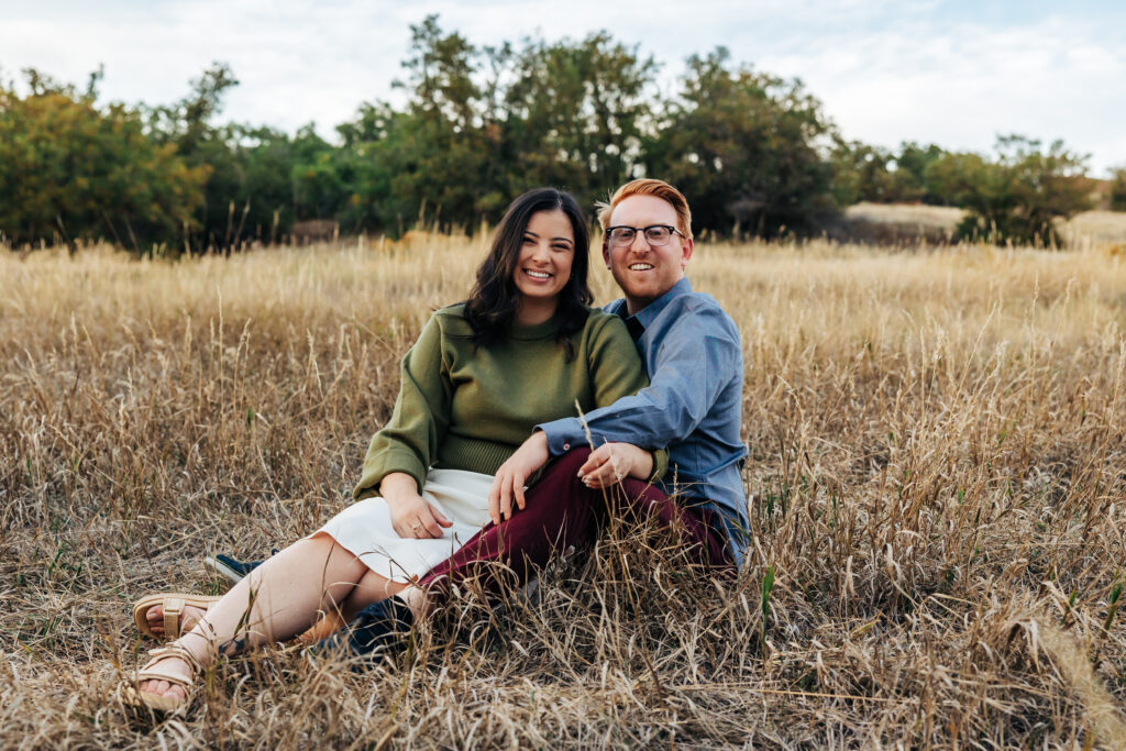 Colorado Elopement Photographer captures newly engaged couple sitting together in grass during fall engagement photos