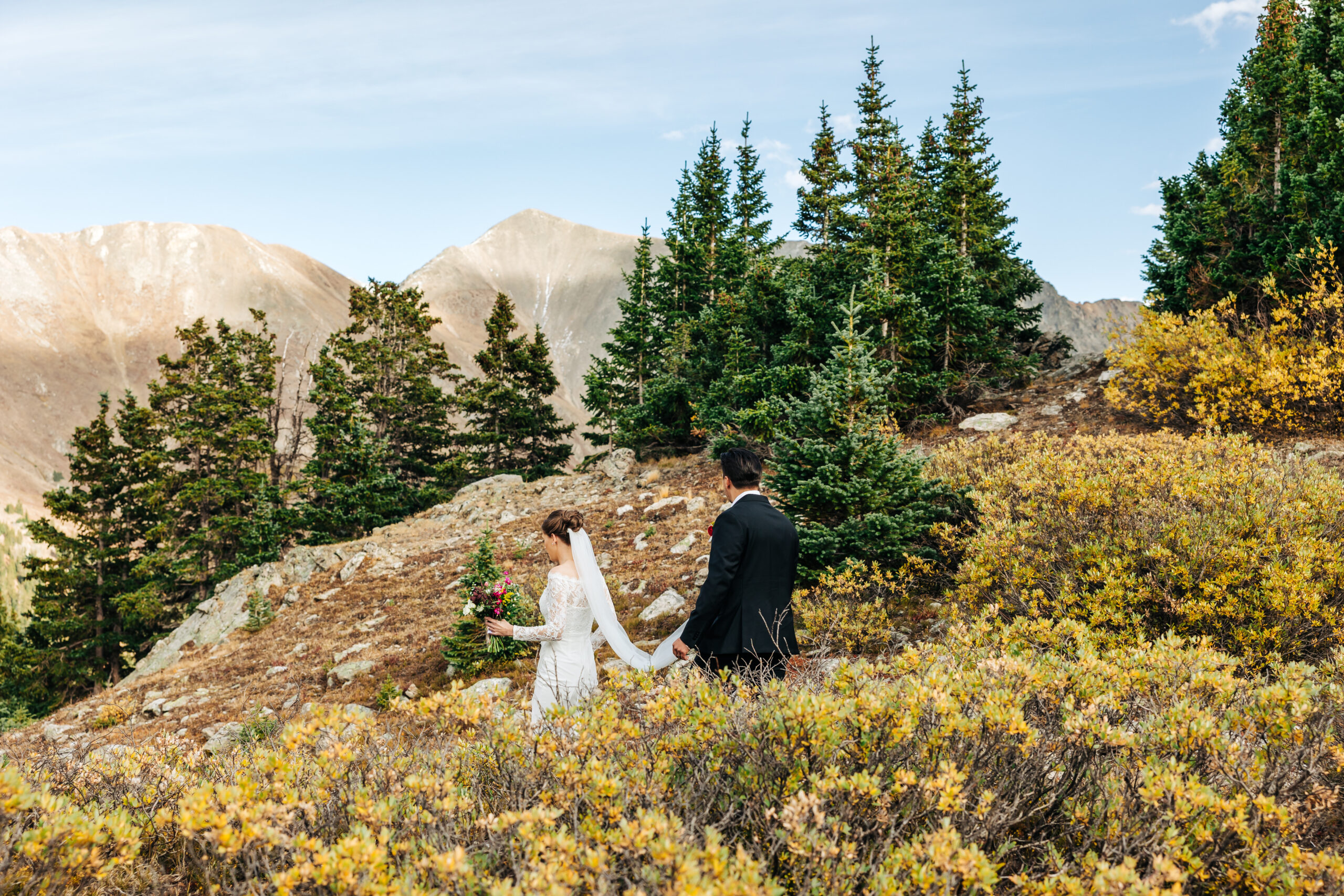 Colorado Elopement Photographer captures bride and groom walking through wildflowers