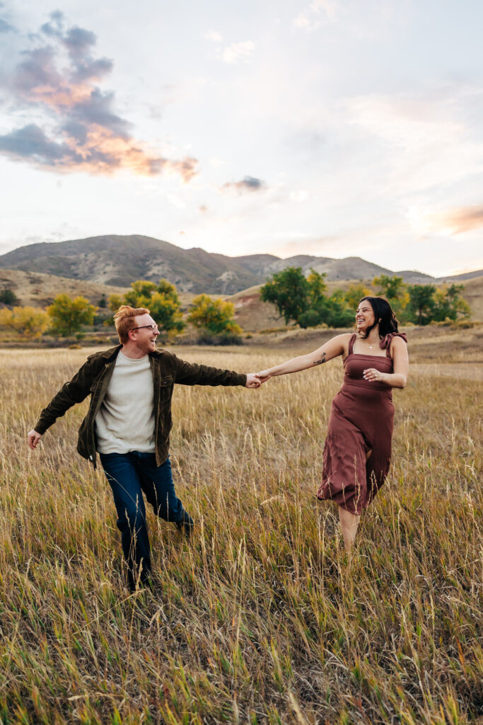 Colorado Elopement Photographer captures engaged couple holding hands and running through field