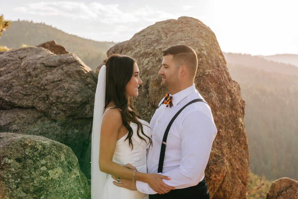 Bride and groom gazing at each other, framed by warm sunlight and mountain boulders.