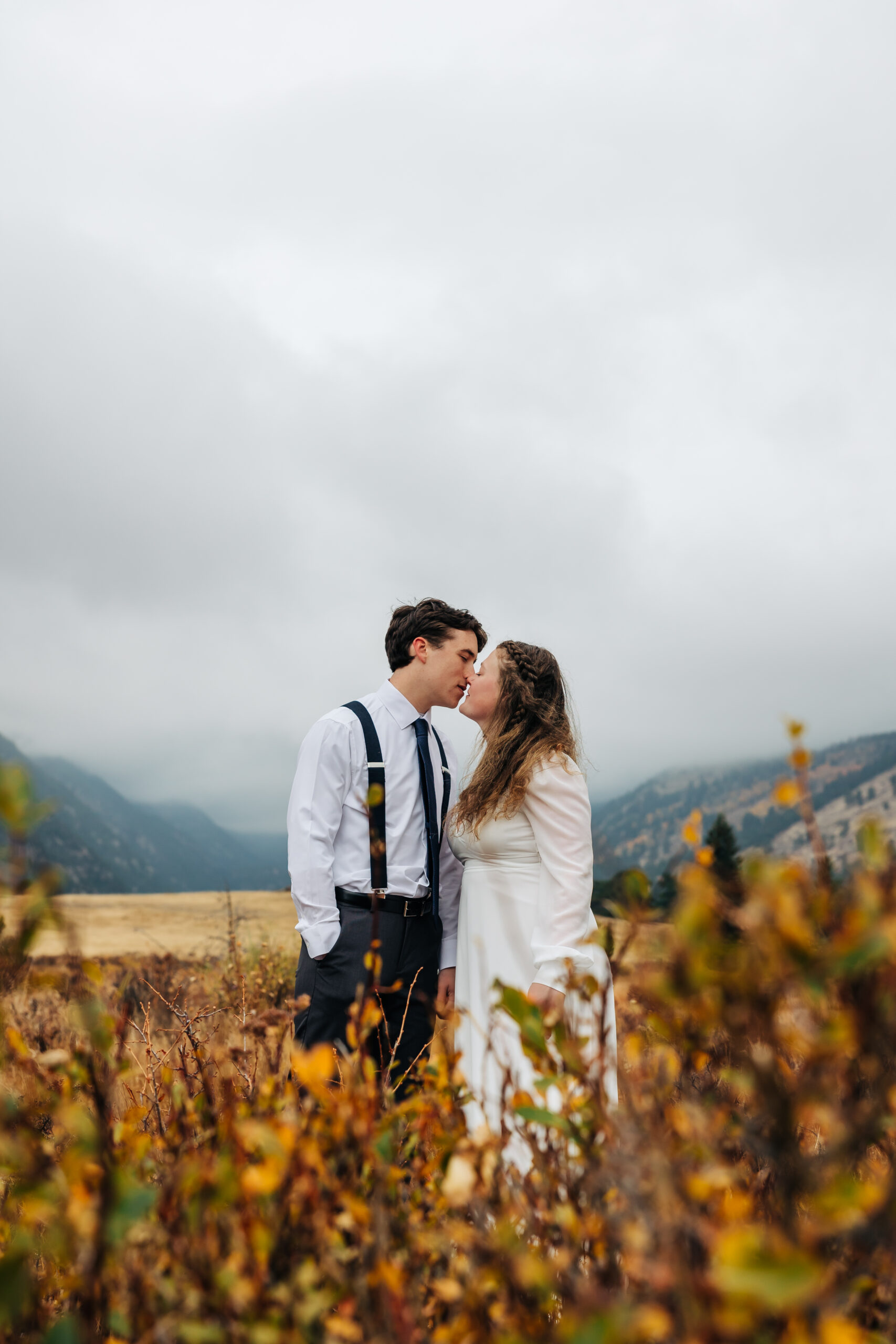 Couple shares a kiss among fall foliage with misty mountains in the background near Boulder, Colorado.