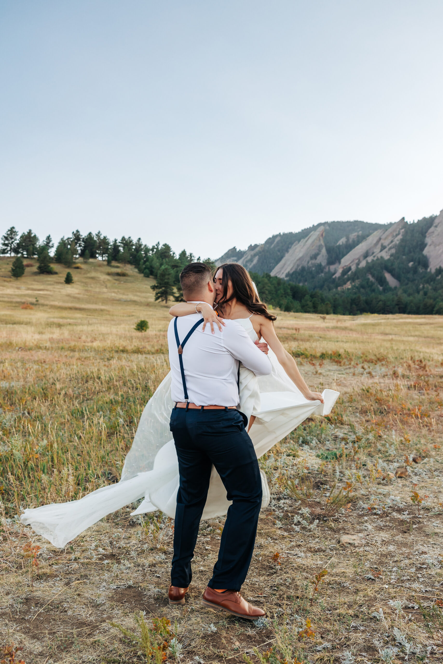 Groom twirls bride in a golden meadow during sunset near Boulder, Colorado.