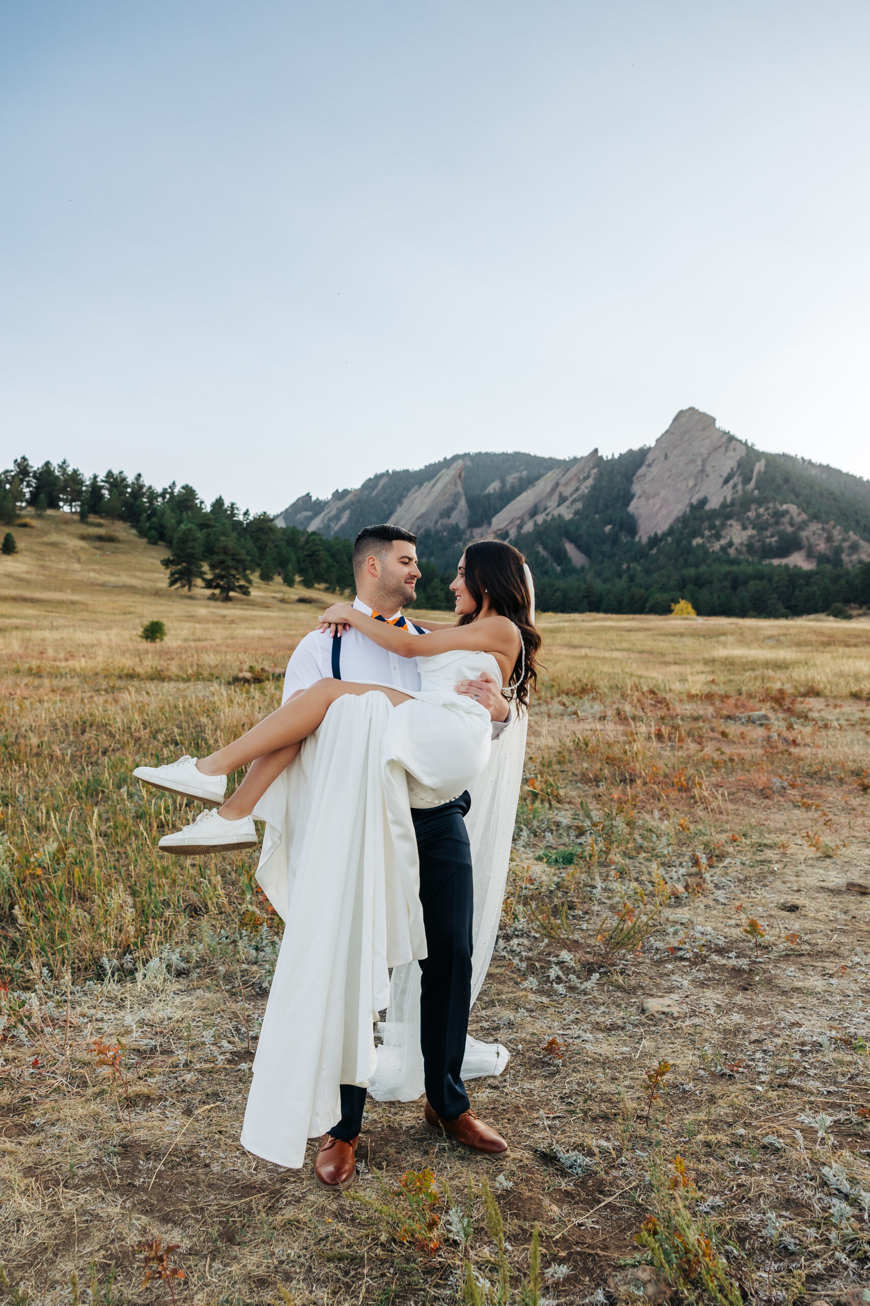 Groom carries bride in a field with the Flatirons in the background — one of our signature Colorado elopement packages.