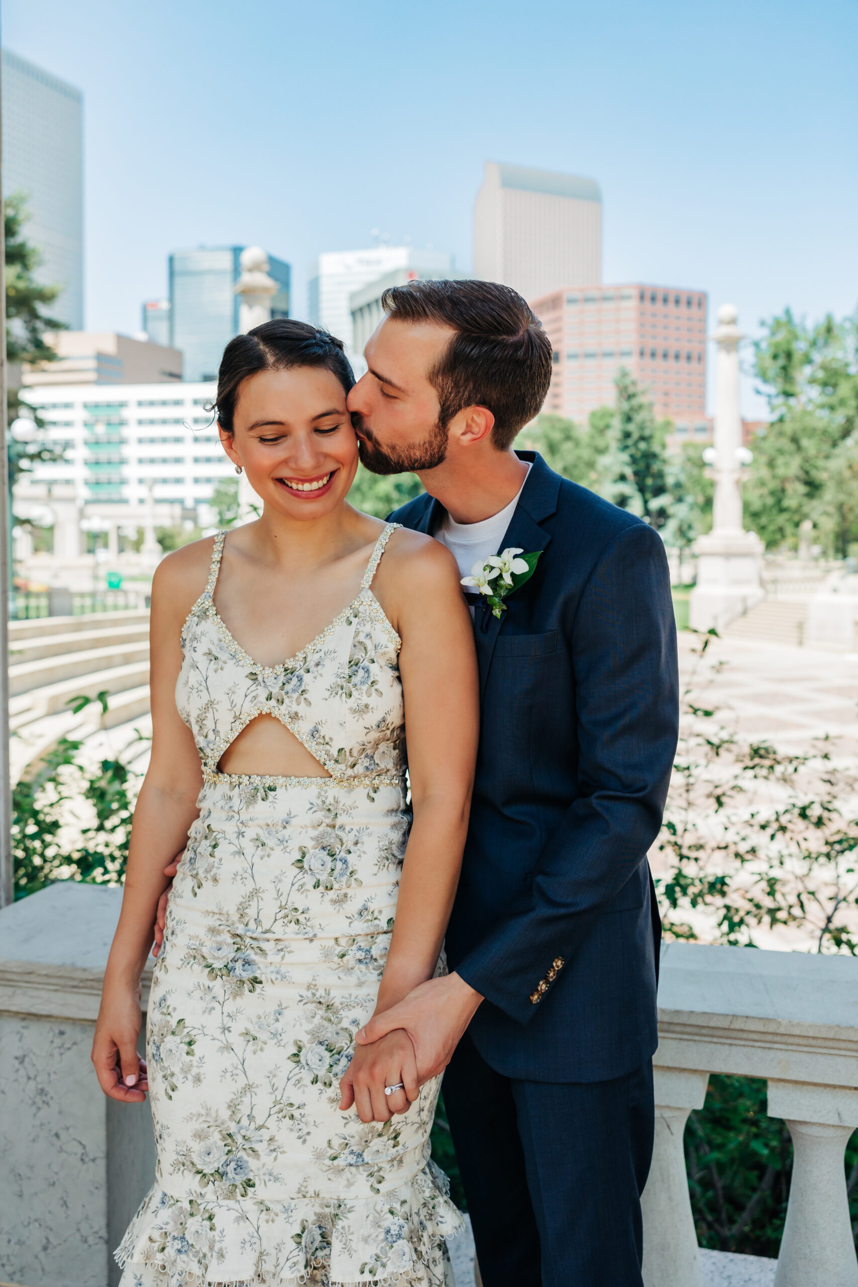 Groom kisses his bride against a backdrop of the Denver skyline—an easy, scenic way to save money for your Colorado elopement without sacrificing beauty.