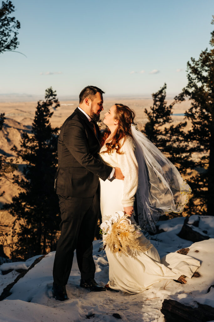 Bride and groom share a romantic moment on a snow-covered overlook during their winter Boulder wedding.