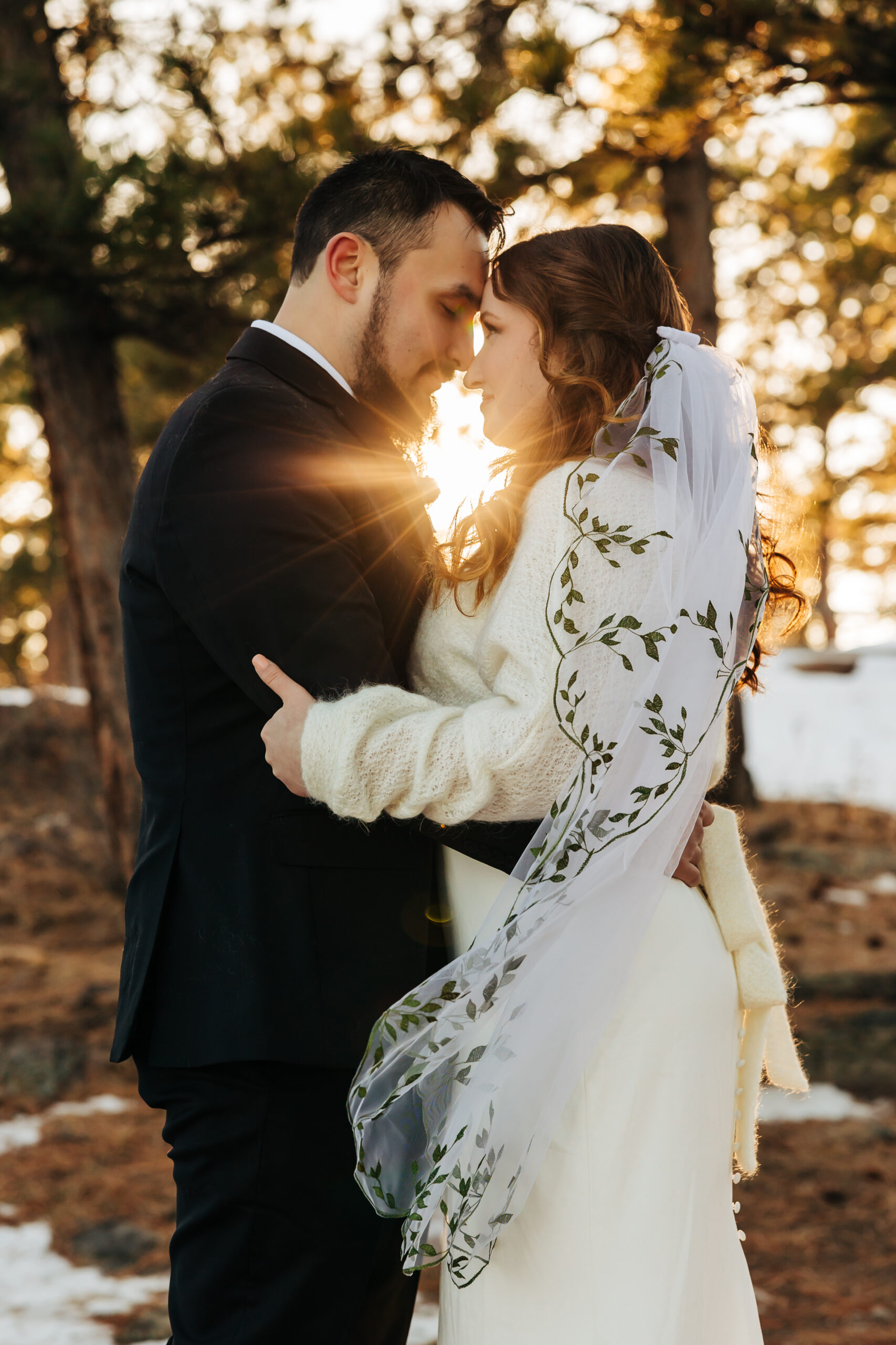 Couple embraces at sunset with golden light streaming between them, wrapped in cozy winter attire at their Boulder wedding.
