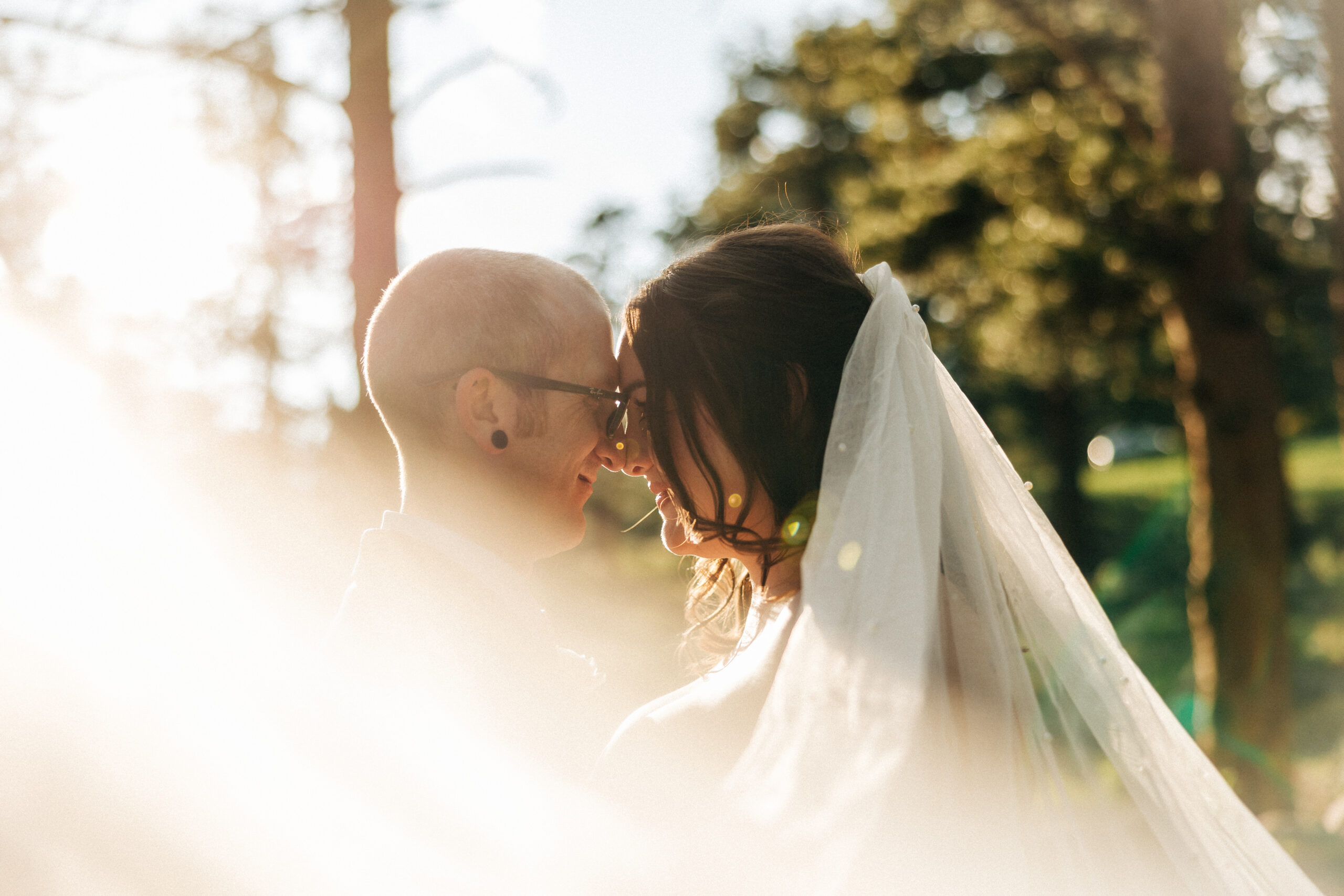 Bride’s veil flows in the breeze as she leans in to nuzzle her partner, with forested mountains rising in the distance.