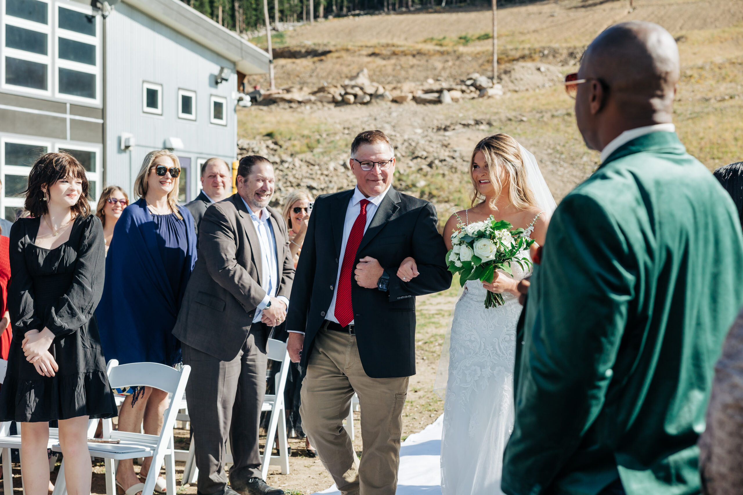 Bride walks down the aisle arm in arm with her father as guests look on during her Colorado mountain wedding ceremony.