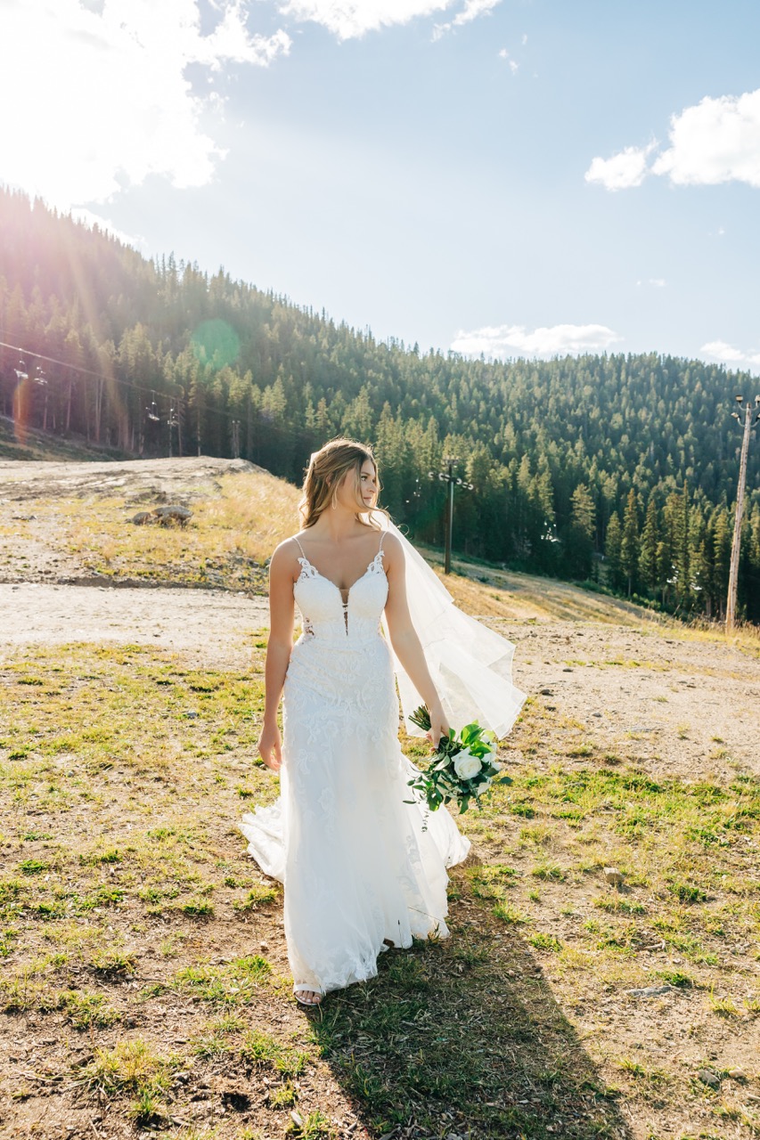 Bride glows in the late afternoon sun, her veil trailing as she poses among the trees during her Colorado mountain wedding.