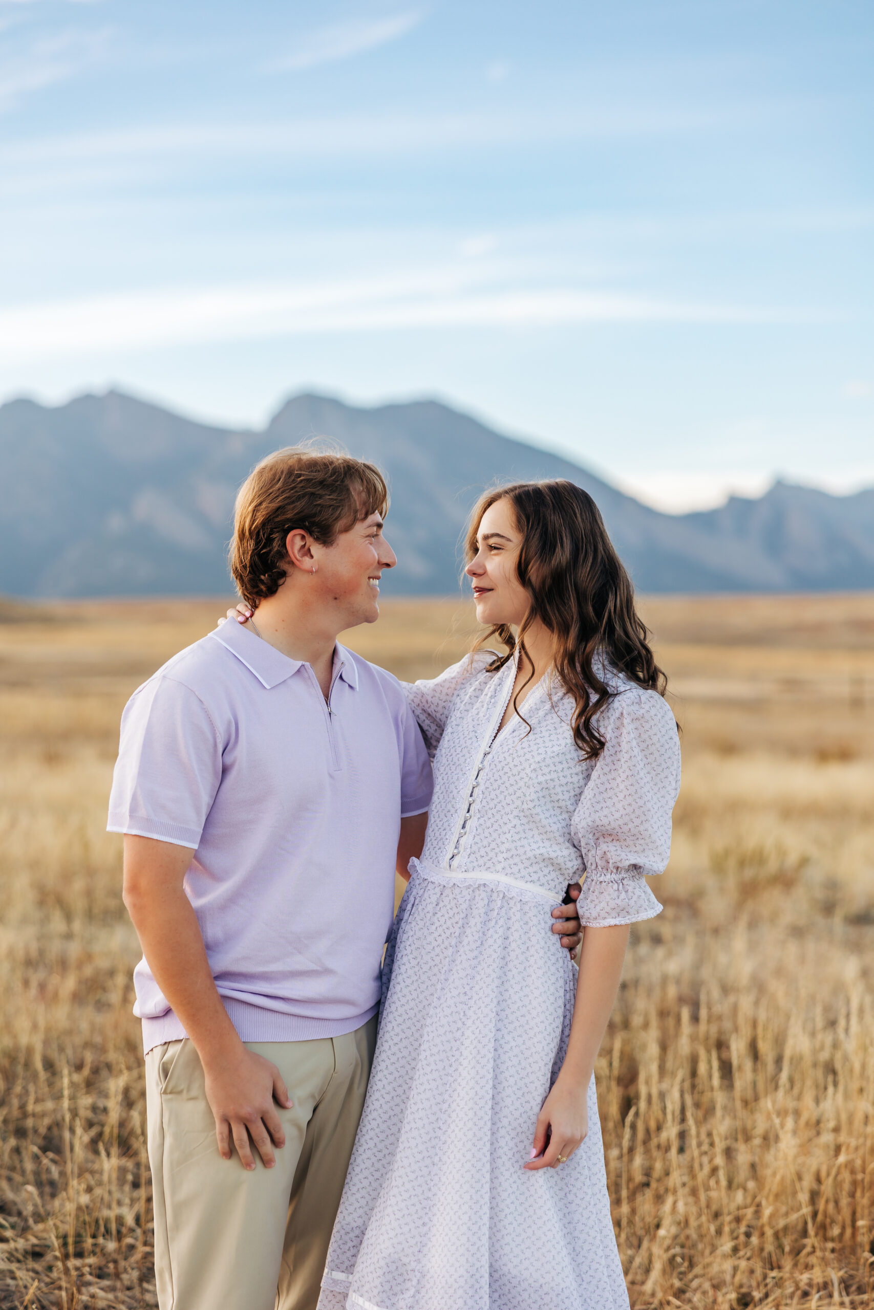 Couple shares a sweet gaze in a sunlit field with the Boulder mountains behind them, a perfect moment from their Boulder engagement photos.