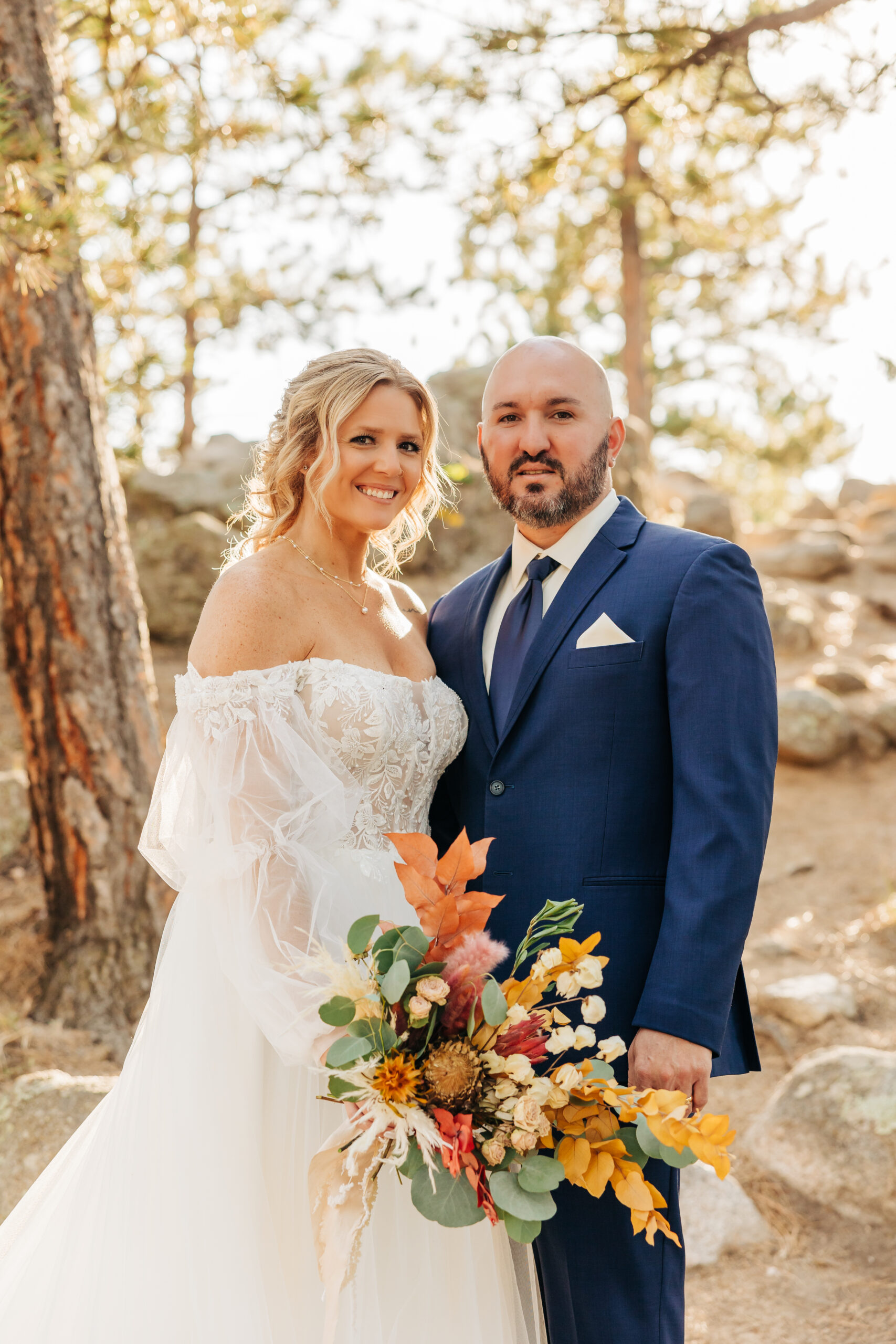 Happy couple smiles for a close-up portrait with golden hour light filtering through the trees, taken by Boulder wedding photographers.
