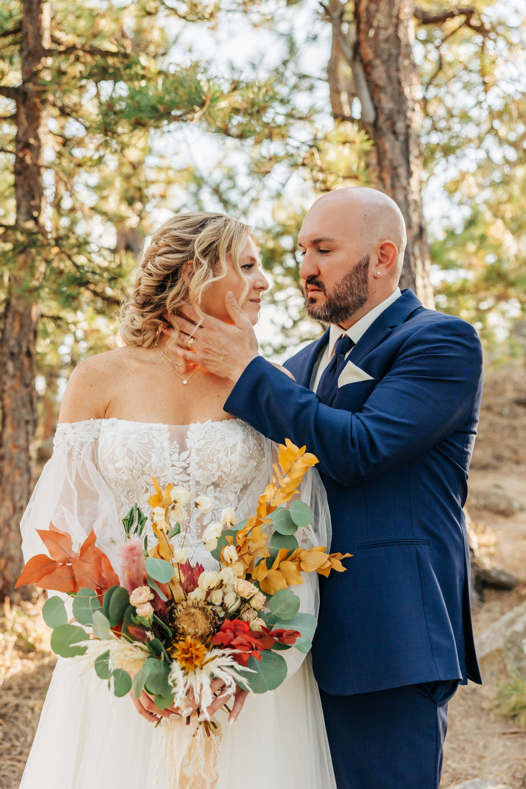 Groom cups his bride’s face during a heartfelt moment, her bold bouquet standing out in this portrait by Boulder wedding photographers.