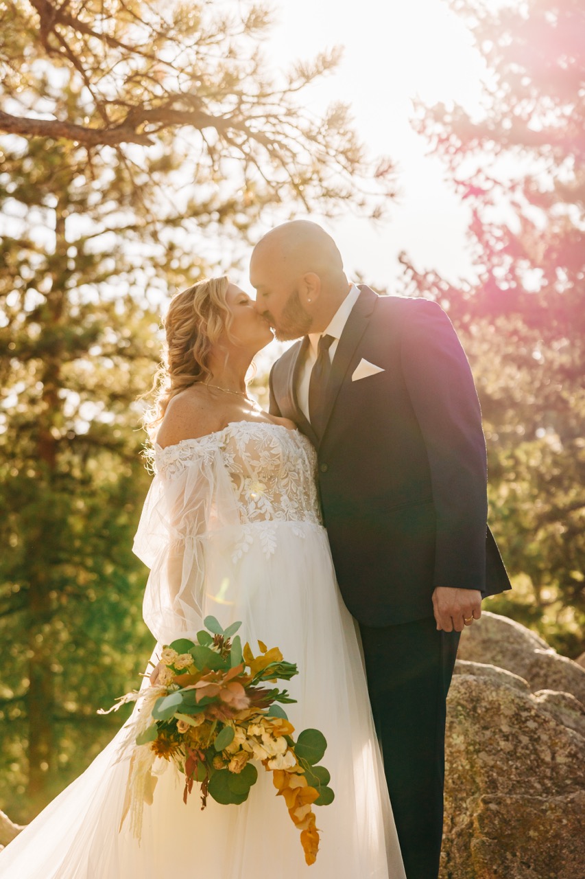 Bride and groom share a romantic kiss at sunset in the Colorado foothills, a moment beautifully captured by Boulder wedding photographers.
