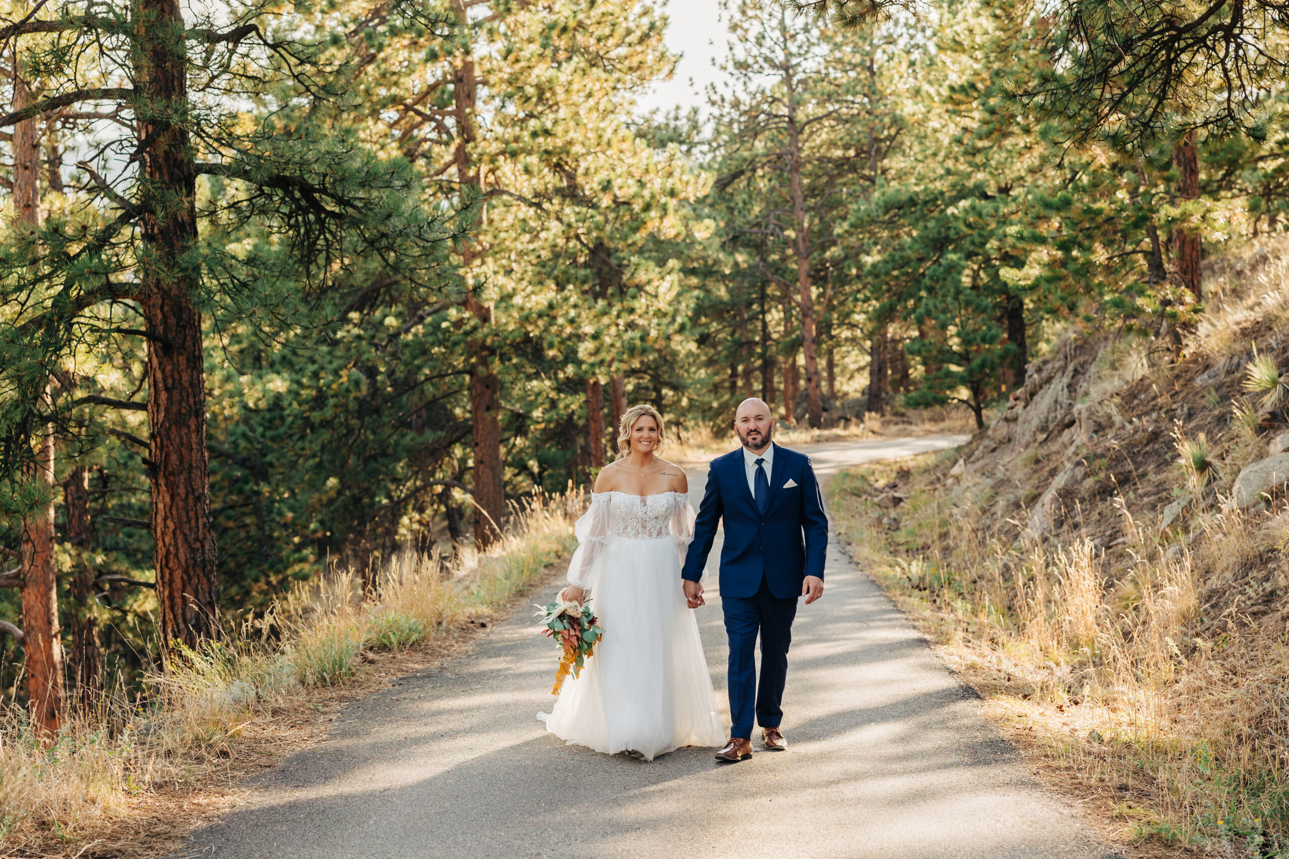 Bride and groom walk a quiet mountain road together after their intimate ceremony, a candid moment preserved by Boulder wedding photographers.