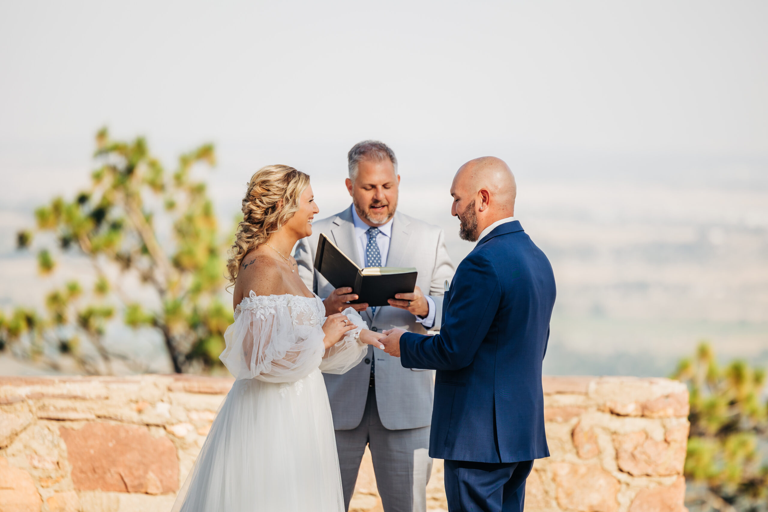 Bride and groom exchange rings during a joyful outdoor ceremony, a genuine moment documented by Boulder wedding photographers.