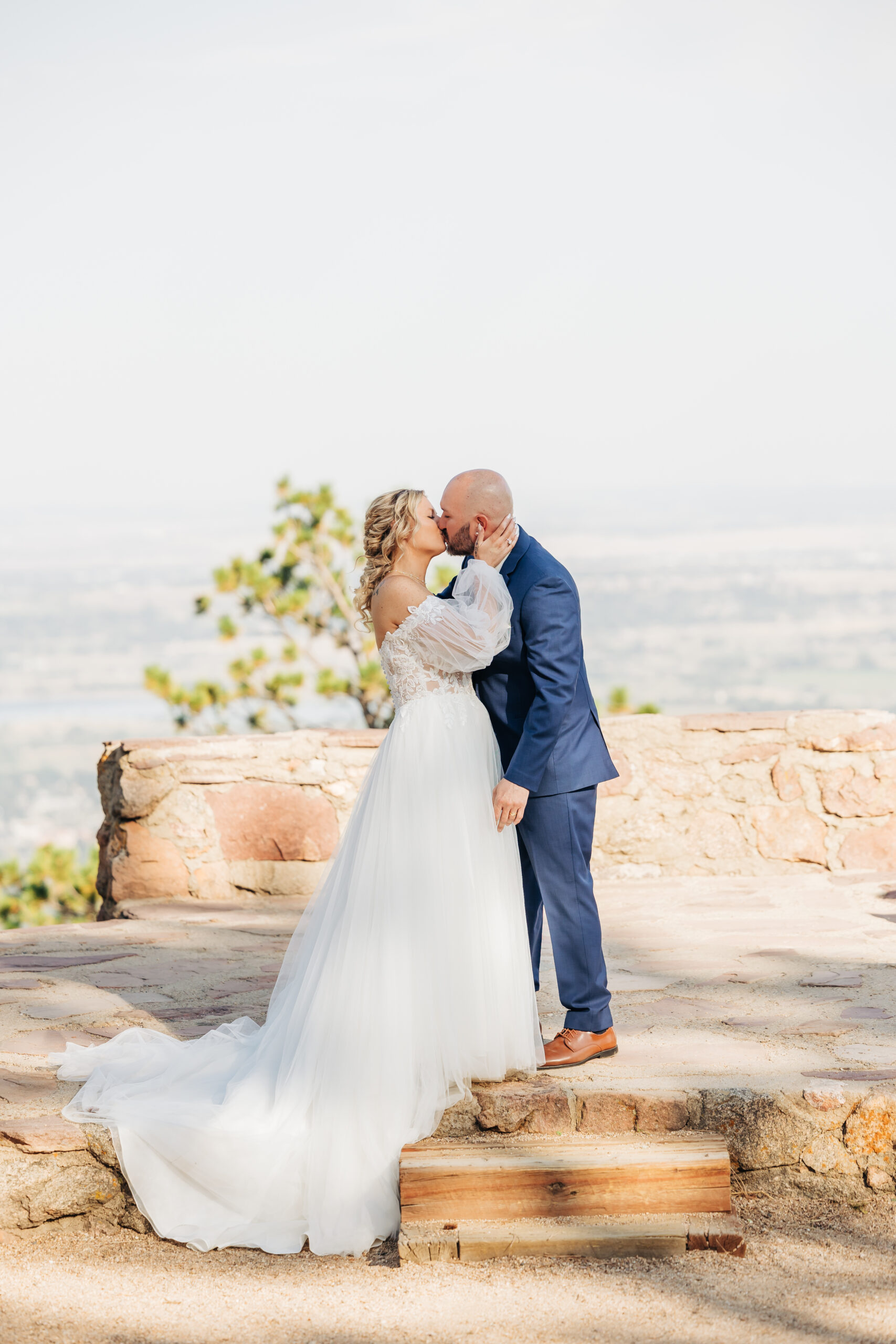 Bride and groom share a kiss on a scenic stone overlook above Boulder, a magical moment captured by Boulder wedding photographers.